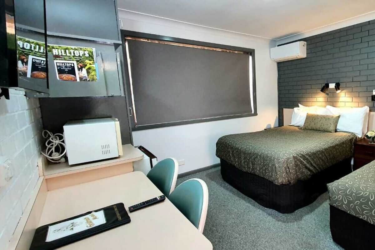 Habitación de hotel con dos camas, un escritorio y una silla. Cuenta con un ventanal grande y una pared de ladrillo.