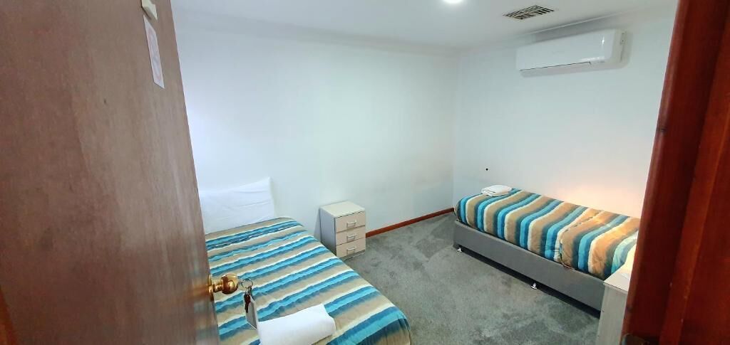 Una habitación pequeña y limpia, con dos camas, un mueble pequeño y un equipo de aire acondicionado en la pared.