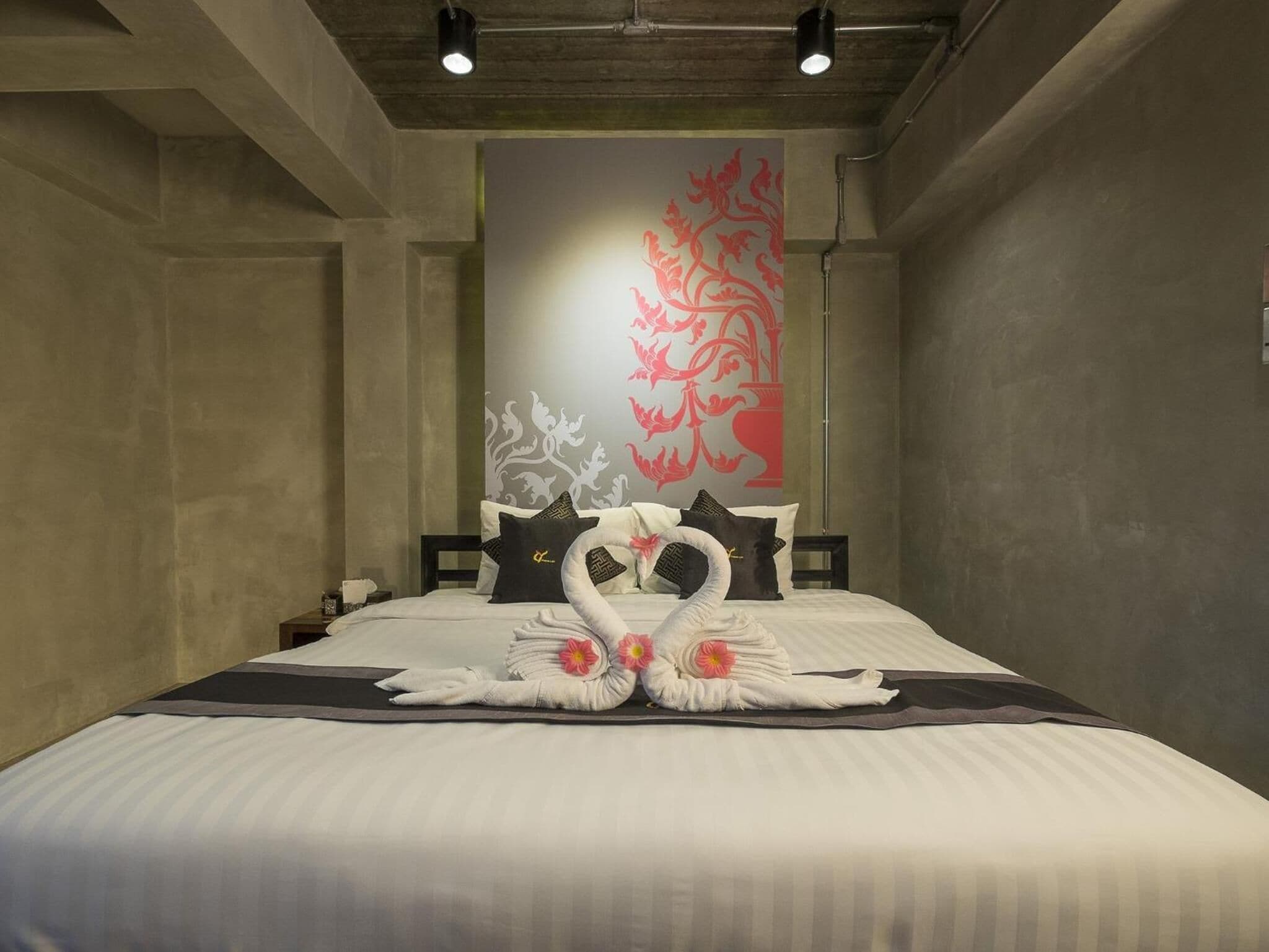 A hotel room with a large bed, a decorative wall with a red floral pattern, and a swan-shaped towel arrangement.