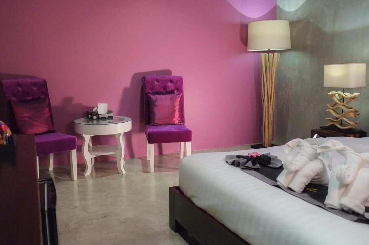 A hotel room with a bed, two purple armchairs, a small round table with a tissue box, and two lamps.