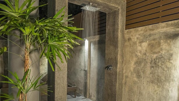 Une douche extérieure moderne, dotée d’une structure en pierre, d’un palmier et d’un sol en béton.