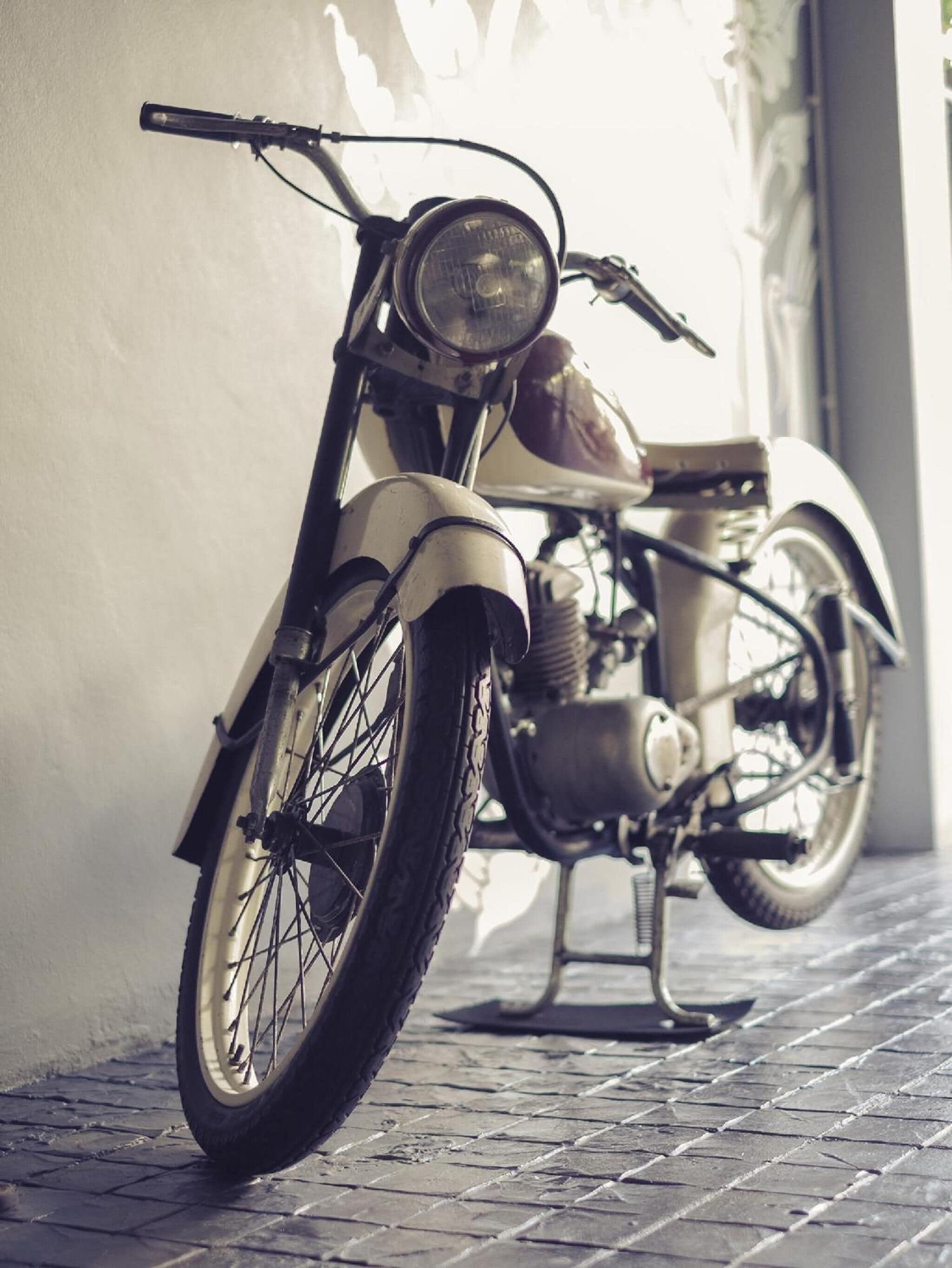 Una motocicleta antigua estacionada junto a una pared sobre superficie adoquinada.