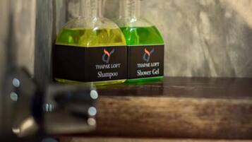 Two bottles of Thapee Loft Shampoo and Shower Gel on a wooden shelf against a textured wall.