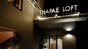 L'entrée de Thapae Loft est marquée par un escalier menant à la porte d'entrée, agrémentée de plantes en pot et d'un espace salon visible à travers les portes vitrées.