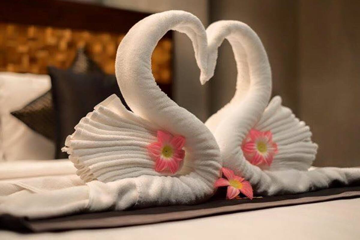 Two swan-shaped towels with pink flowers on a bed.