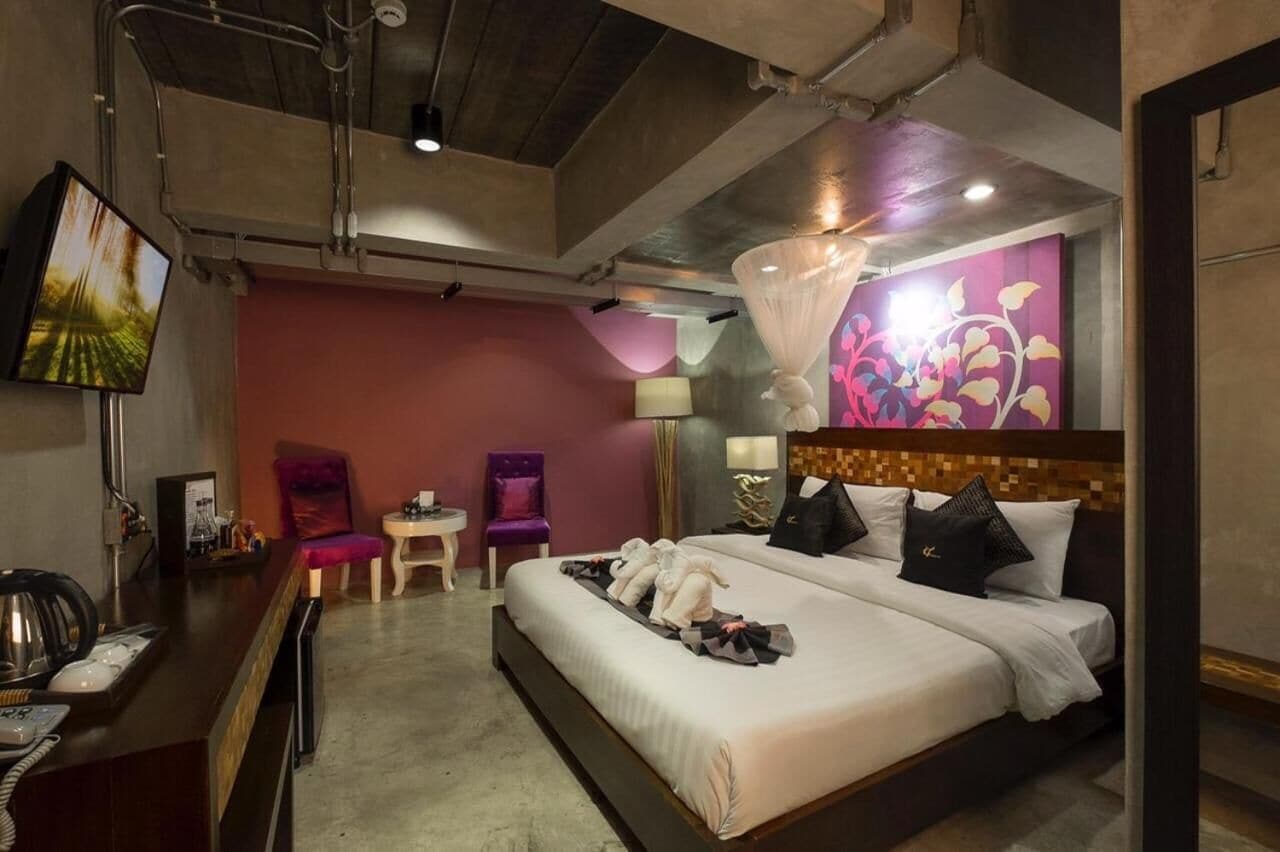 Ein Hotelzimmer mit einem großen Bett, einem Schreibtisch mit Telefon, einem Sessel, einem kleinen Tisch und einem an der Wand befestigten Fernseher.