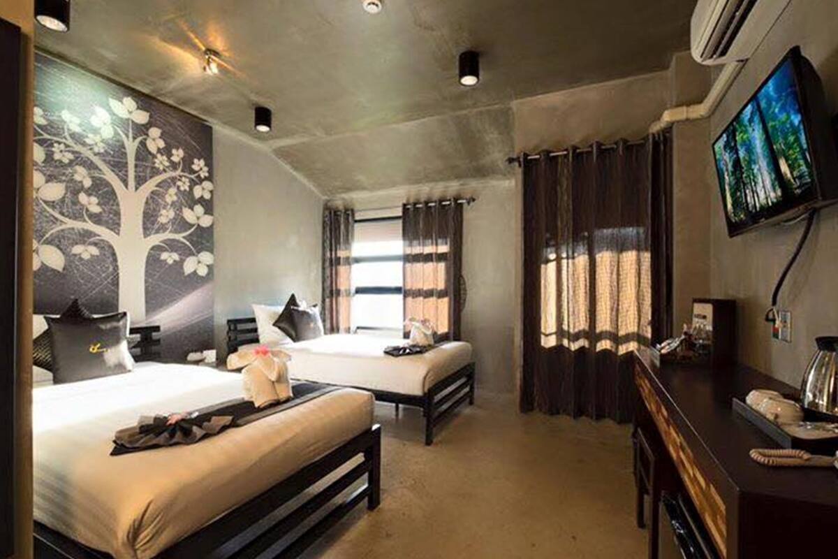 A hotel room with two beds, a flat-screen TV, a desk with a telephone, and a wall-mounted air conditioner.