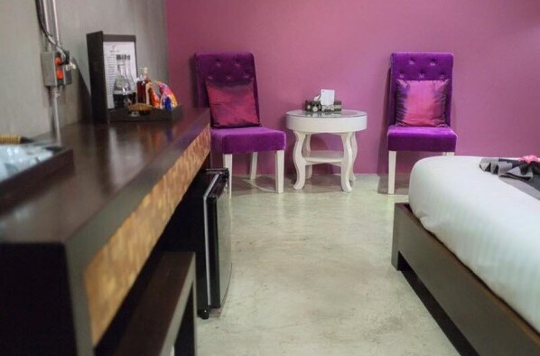 Une chambre d’hôtel avec un lit, un bureau, deux chaises violettes et une petite table ronde.