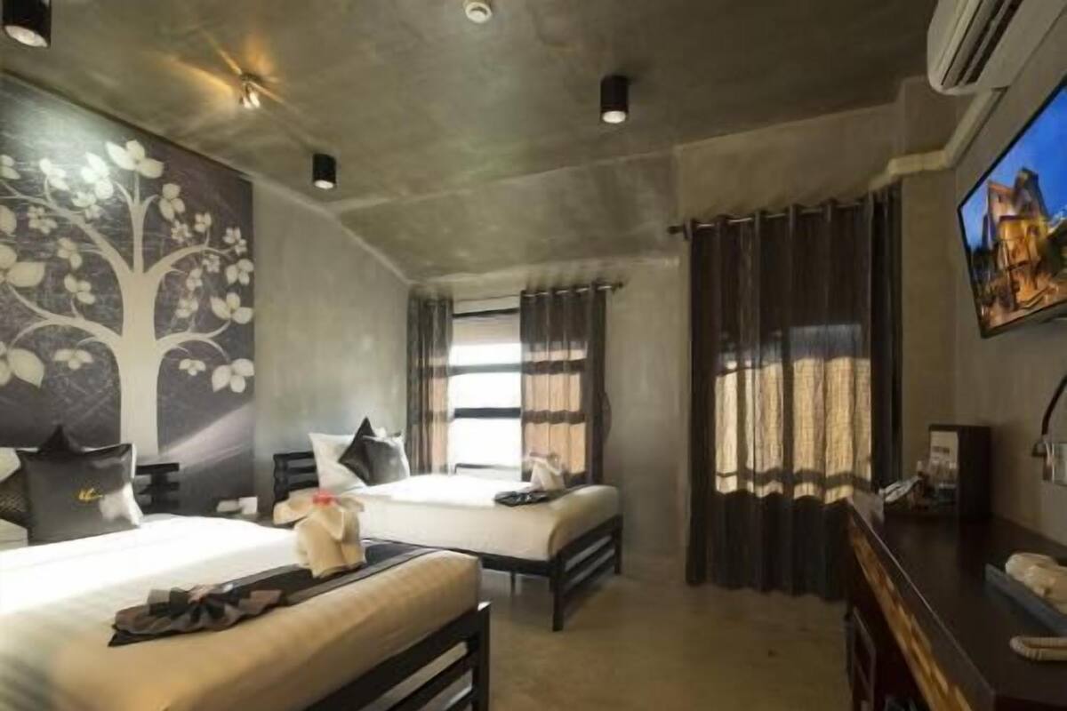 A hotel room with two beds, a desk, a TV, and a large window with curtains.