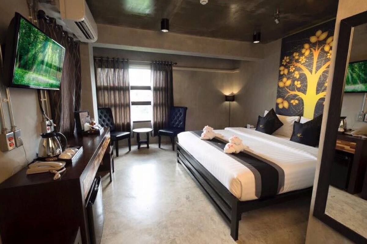 A hotel room with a bed, a desk with a telephone, a chair, a television, and a wall-mounted air conditioner.