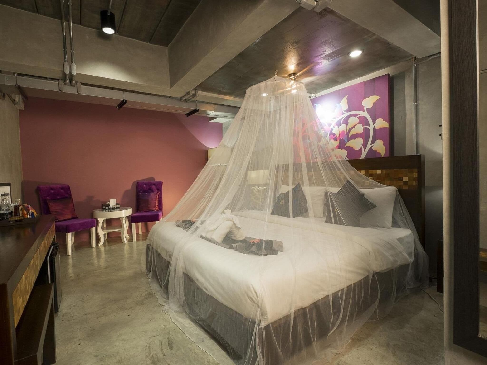 Une chambre à coucher avec un lit recouvert d’un dais en voile léger, une petite table avec une chaise et un mur orné d’un motif floral.