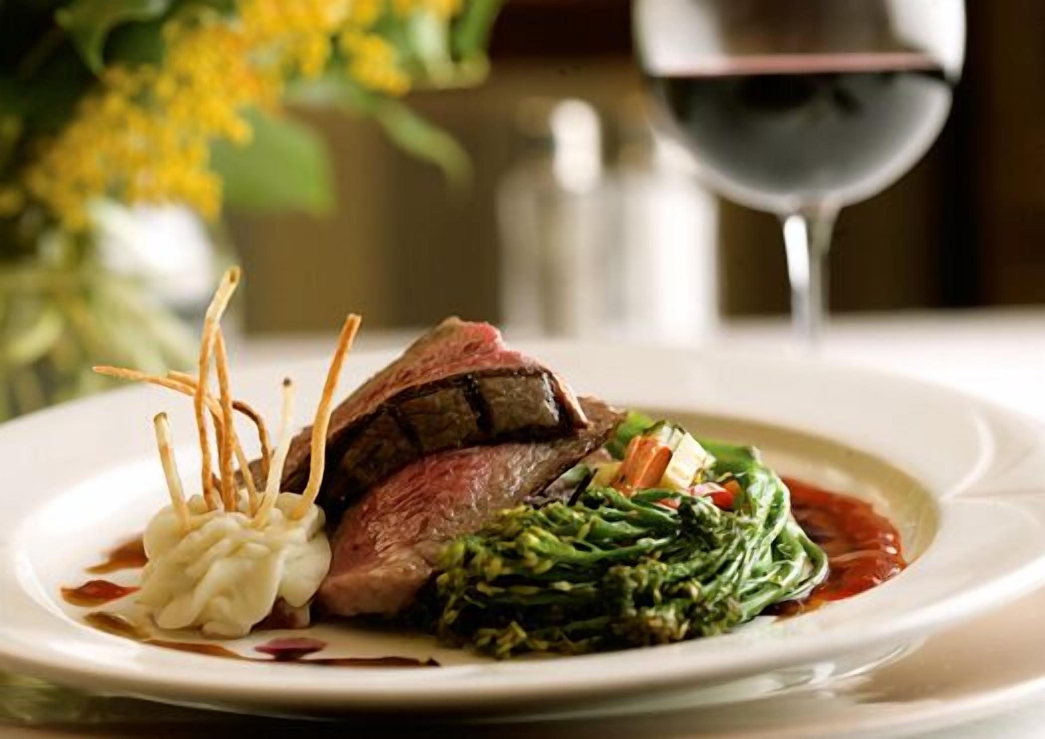 A plate of food with a steak, vegetables, and a glass of red wine.