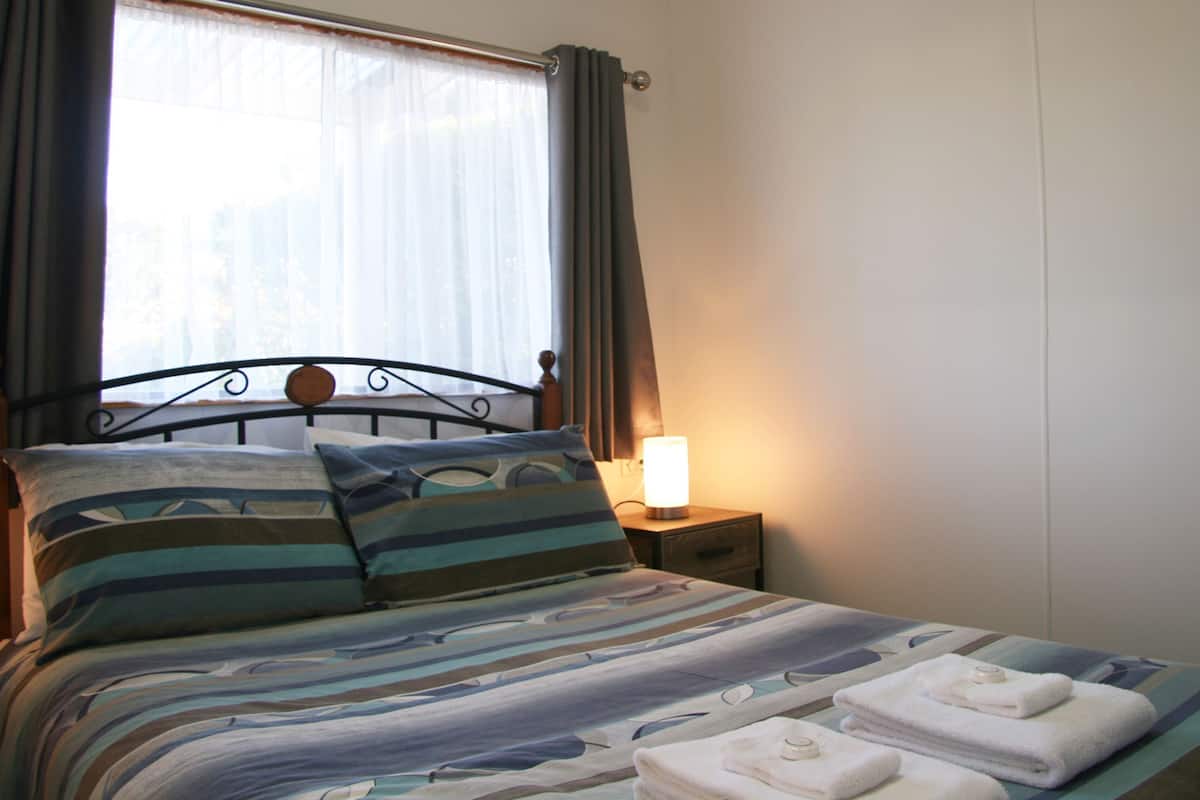Un lit avec une literie à rayures, une lampe de chevet et une fenêtre avec des rideaux.
