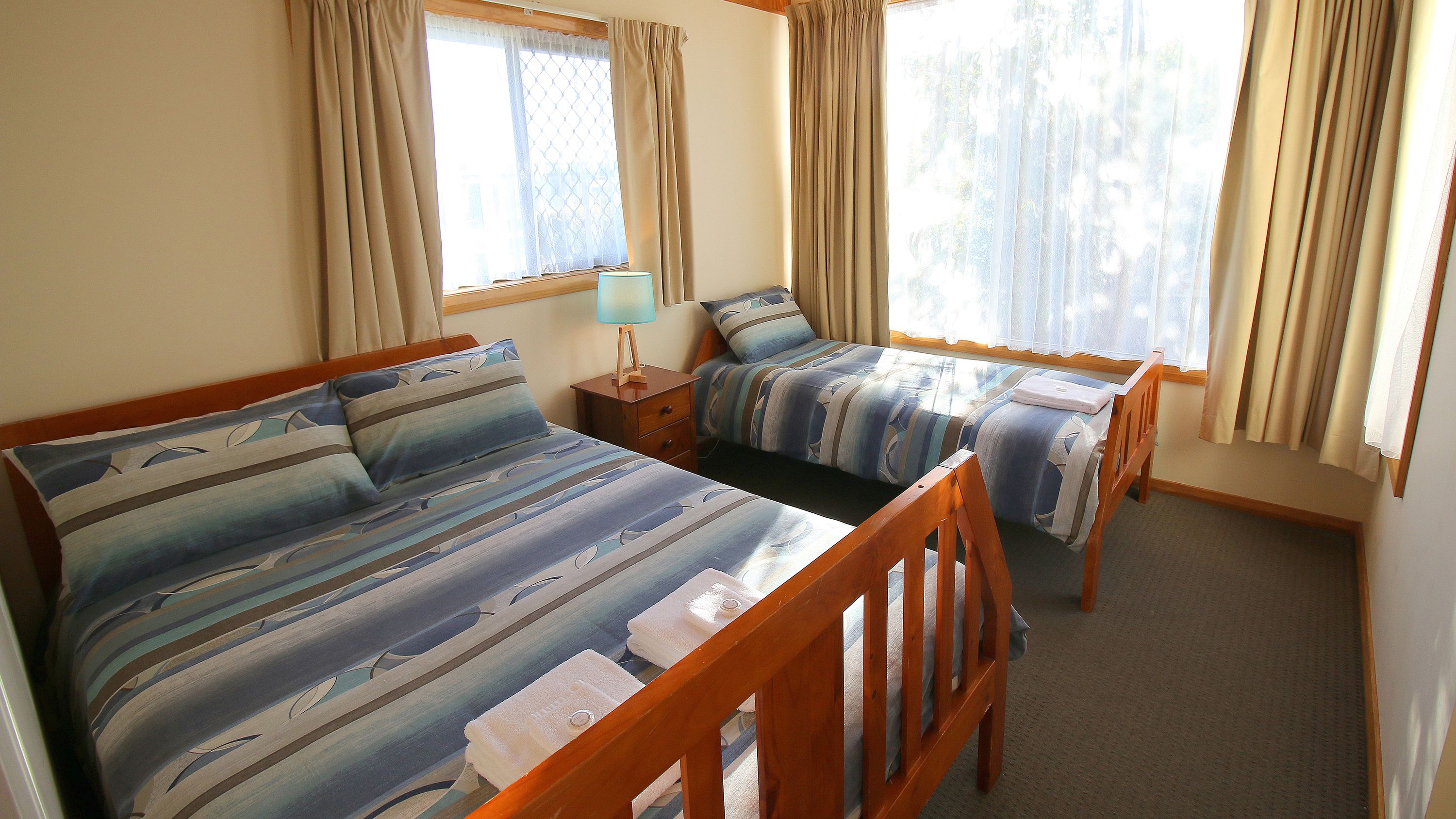 Una habitación con dos camas individuales, una mesita de noche con lámpara y una ventana con cortinas.