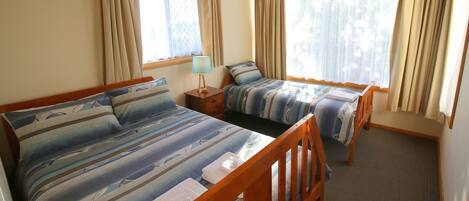 Une chambre avec deux lits simples, une table de chevet avec une lampe et une fenêtre avec des rideaux.