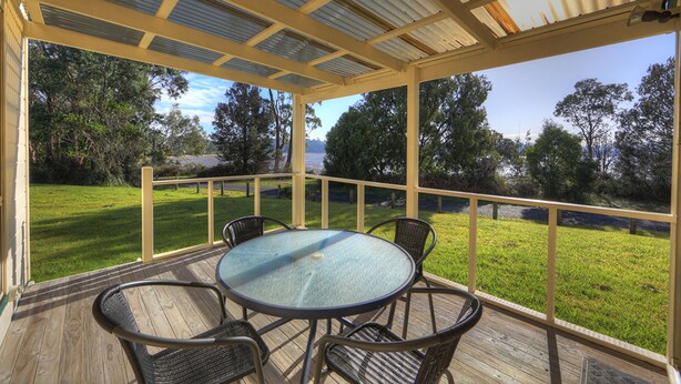 Zona exterior coberta amb taula rodona i quatre cadires, envoltada per un terra de fusta i una barana de vidre.