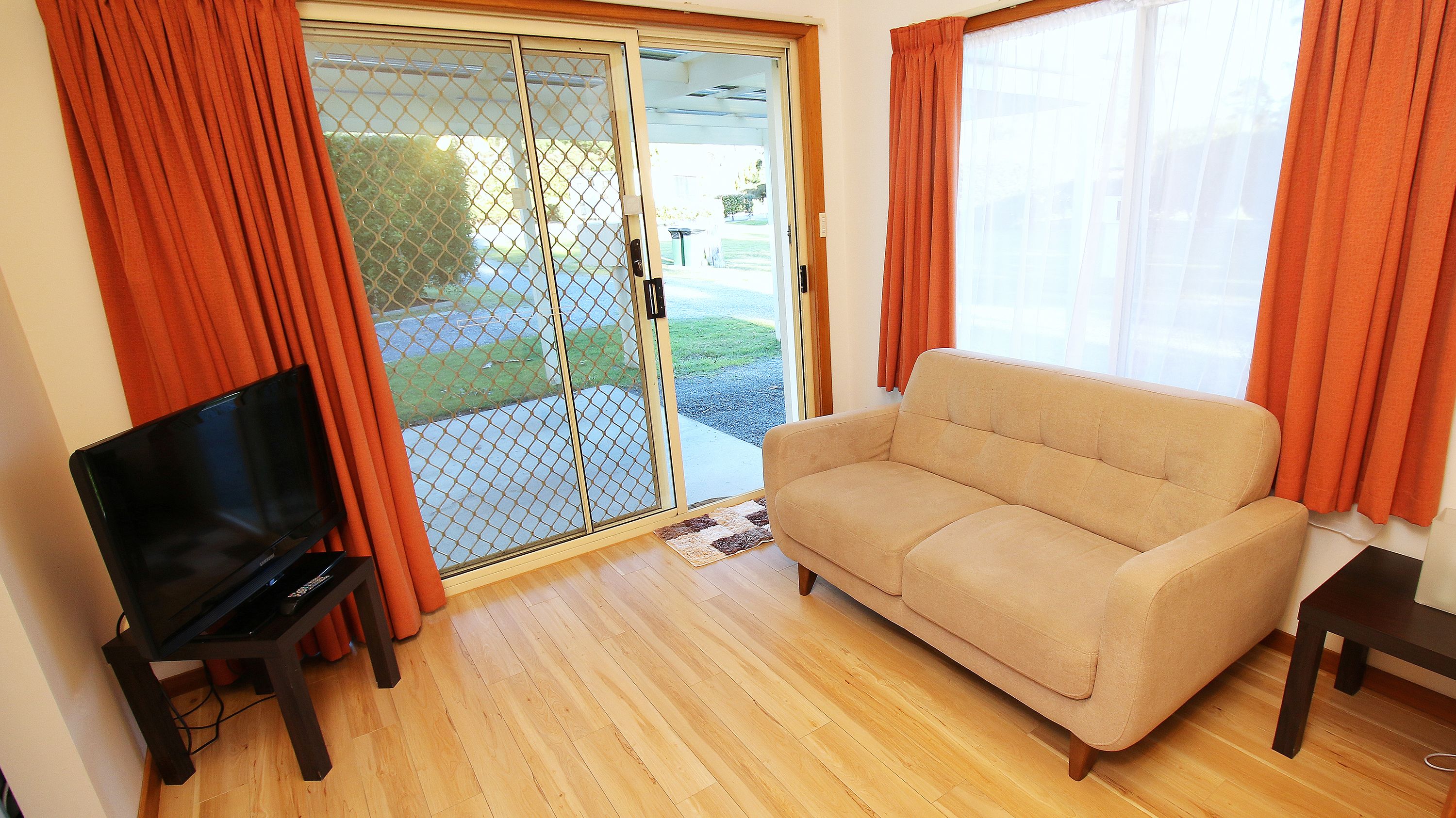 A living room with a beige sofa, a television on a stand, and a sliding glass door leading to a patio.