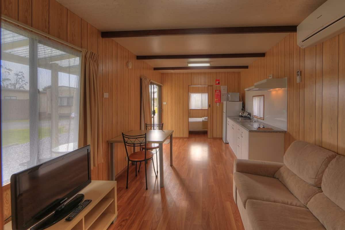 Une pièce compacte avec un intérieur en bois, un canapé, une télévision, une table à manger avec des chaises, un coin cuisine et une porte coulissante donnant sur un espace extérieur.