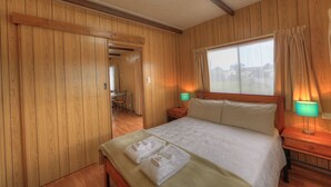 Una habitació amb panells de fusta, un llit, dues làmpades de nit i una finestra amb cortines.