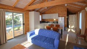 Una cabana acollidora amb zona de estar que inclou un sofà blau, taula de dinar amb cadires, cuina amb armaris blancs i una porta corredissa de vidre que dona a una terrassa exterior.
