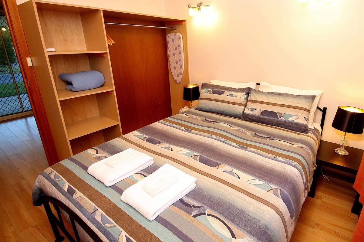 Un lit bien fait, avec une literie à rayures, une armoire en bois et deux lampes de chevet.
