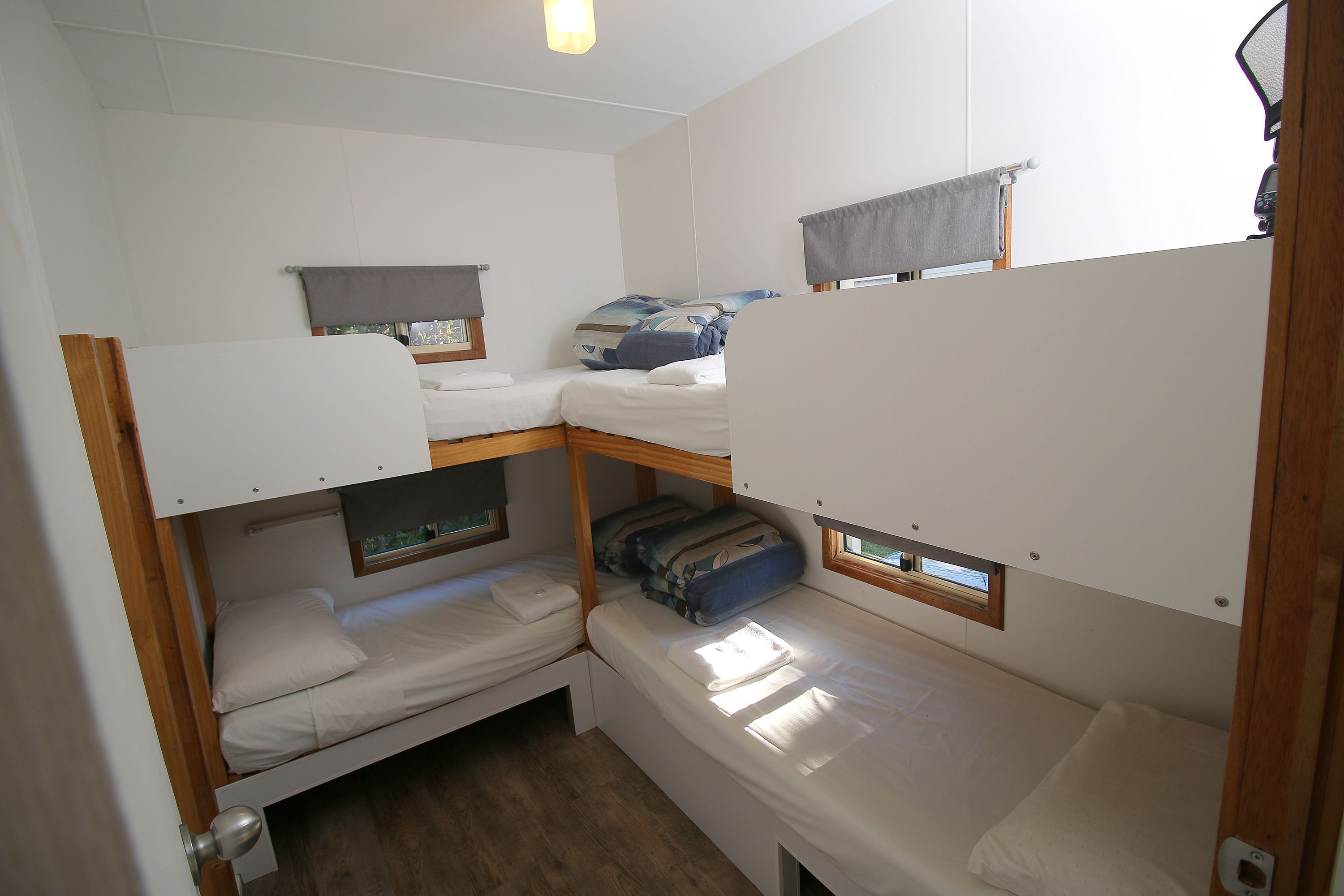 Une pièce compacte et bien éclairée, avec des lits superposés, une petite fenêtre et une porte en bois.