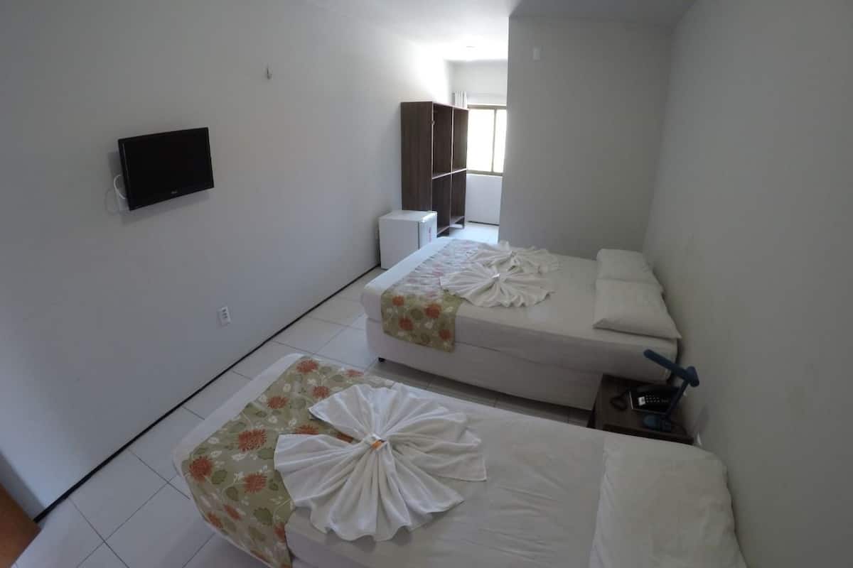 A hotel room with two beds, a TV, a wardrobe, and a small table with a lamp.