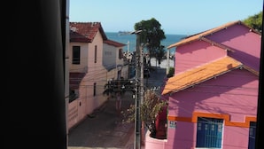 A street view with a pink building, a parked car, and a clear view of the sea. - Iracema Mar Hotel (Fortaleza)