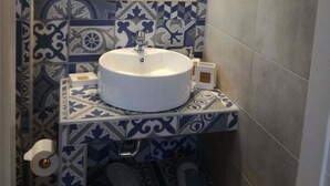 Casa de banho com lavatório branco, azulejos estampados, espelho e porta-toalhas.