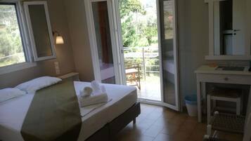 Quarto de hotel com cama, escrivaninha, cadeira, banheiro e porta de vidro corrediça para uma varanda.