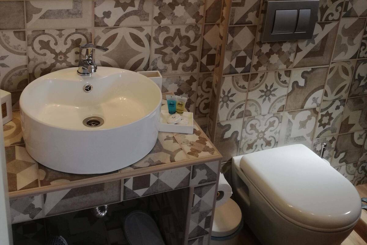 A bathroom with a white sink, a mirror, a toilet, and patterned tiles.