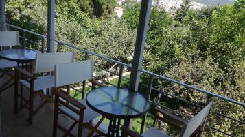 Uma varanda com mesa e cadeiras de vidro, com vista para uma paisagem verdejante e uma cidade distante.