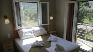 Quarto de hotel com cama, duas mesas de cabeceira, janela e vista para o verde lá fora.