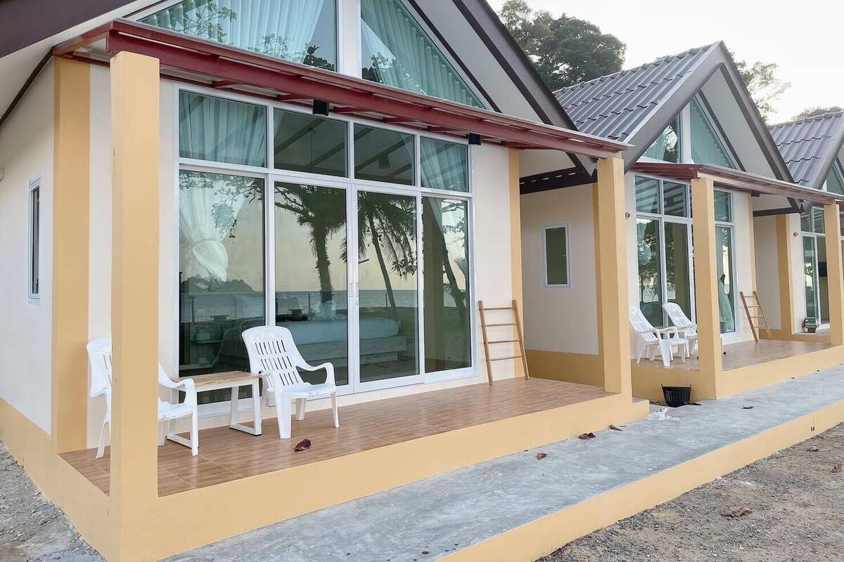 Un edificio moderno con amplios ventanales de vidrio, sillas de plástico blanco y una terraza de madera.