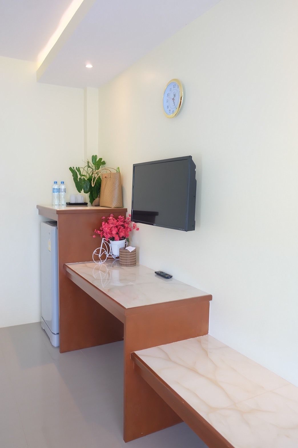 Un moderno mostrador de recepción con un televisor de pantalla plana, un reloj y una pequeña planta.