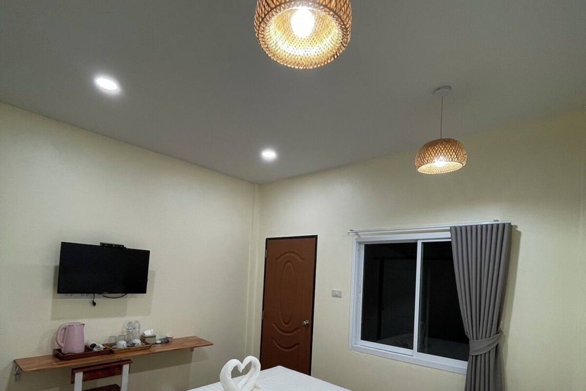 Habitación de hotel con cama, escritorio con televisor, ventana con cortinas y dos lámparas colgantes.