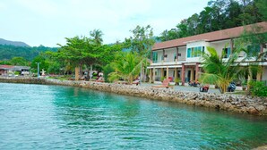 Hotel amb vistes al mar, una paret de pedra, palmeres i aigua cristal·lina.