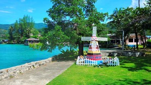 Una estructura de molí de vent colorida amb un rètol que diu "Chokdee Resort", envoltada de vegetació exuberant i un llac blau i tranquil.