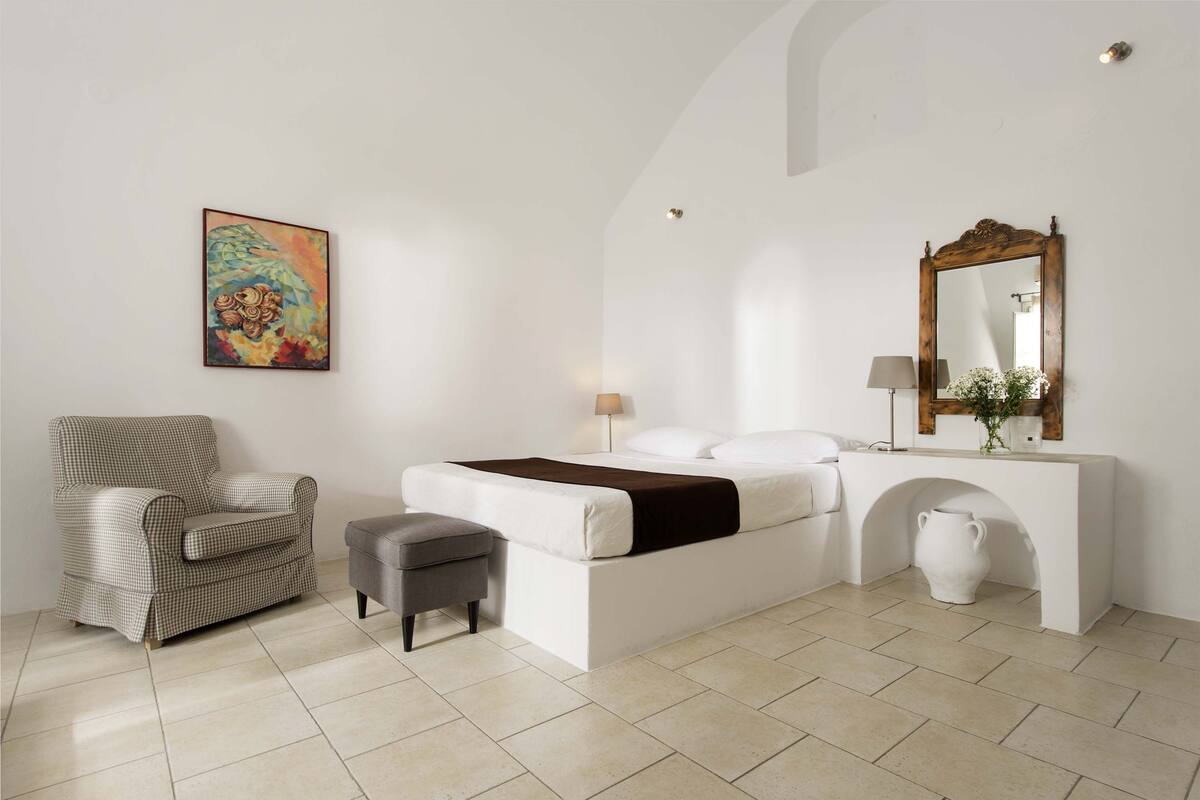 A bedroom with a bed, a chair, a small table, and a painting on the wall.