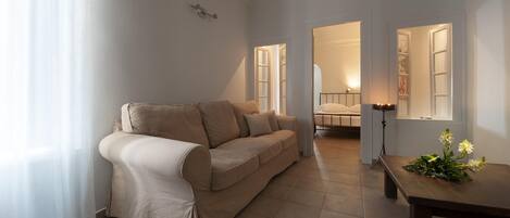 Una sala de estar con un sofá color beige, una mesa de centro de madera con flores, y una lámpara.