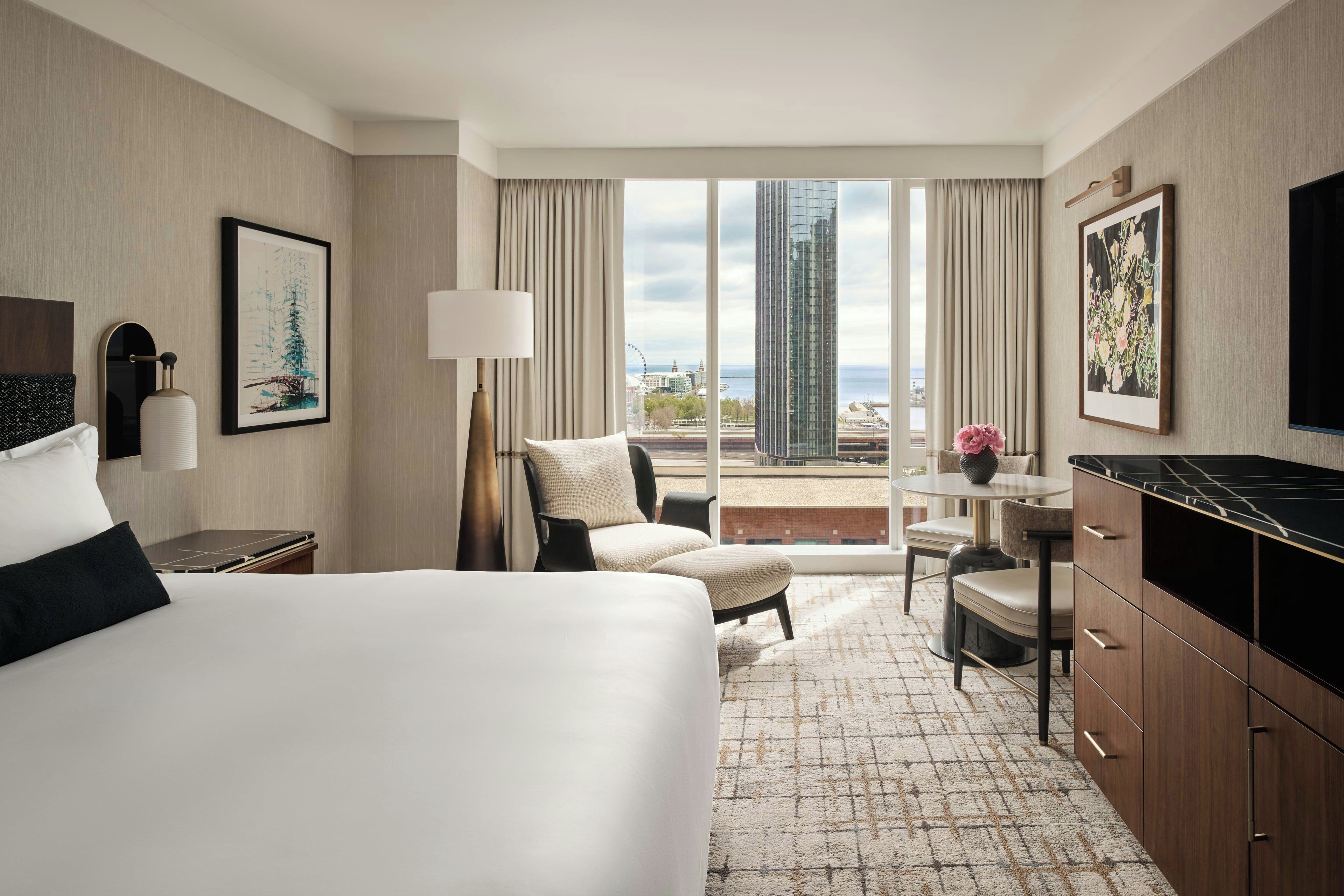A hotel room with a bed, a desk, a chair, a TV, and a view of the cityscape.