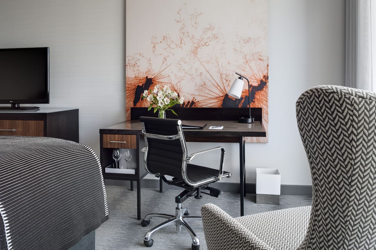 Hotellihuone, jossa on sänky, työpöytä tietokoneella, tuoli ja televisio.