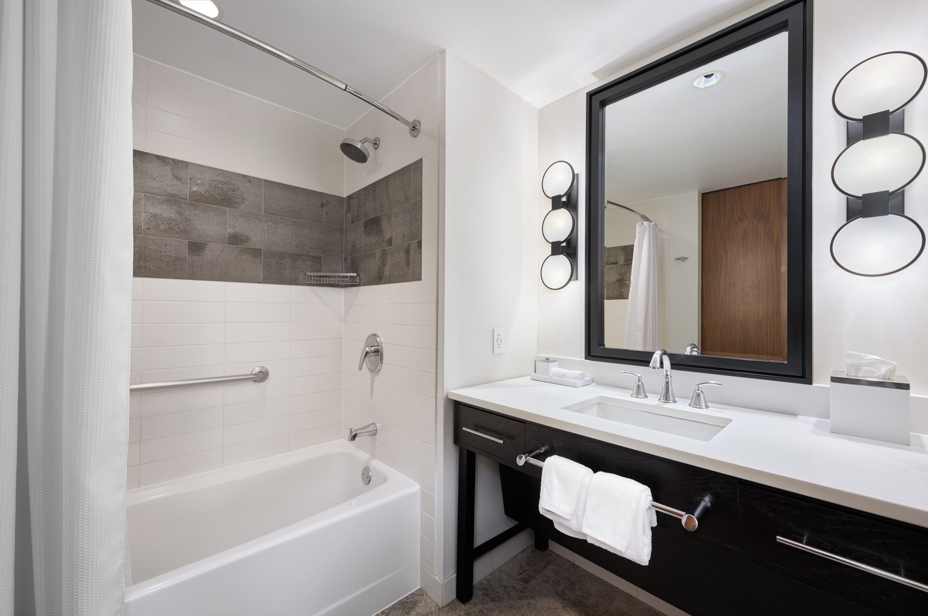 Un baño moderno con bañera, ducha, tocador con espejo y barra para toallas.