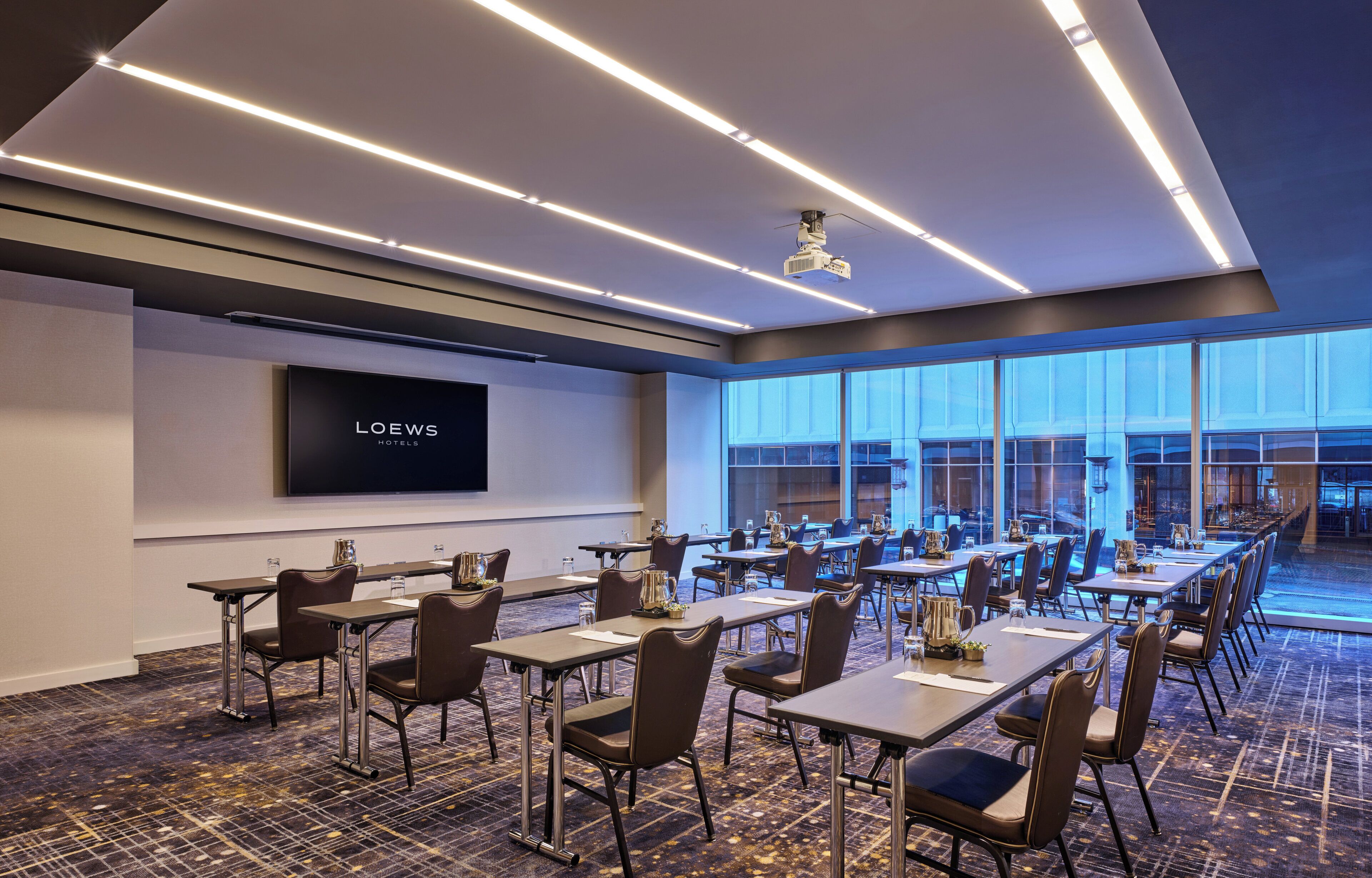 A conference room with a large screen displaying "LOEWS HOTEL" and a long table with chairs.