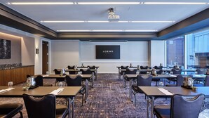 A conference room with tables, chairs, a projector, and a screen displaying "LOEWS HOTELS". - Loews Chicago Hotel (Chicago)