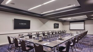 A conference room with a long table, chairs, a projector screen, and a flat-screen TV displaying "LOEWS HOTELS". - Loews Chicago Hotel (Chicago)