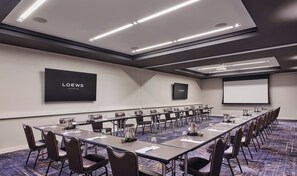 A conference room with a long table, chairs, a projector screen, and a flat-screen TV displaying "LOEWS HOTELS". - Loews Chicago Hotel (Chicago)
