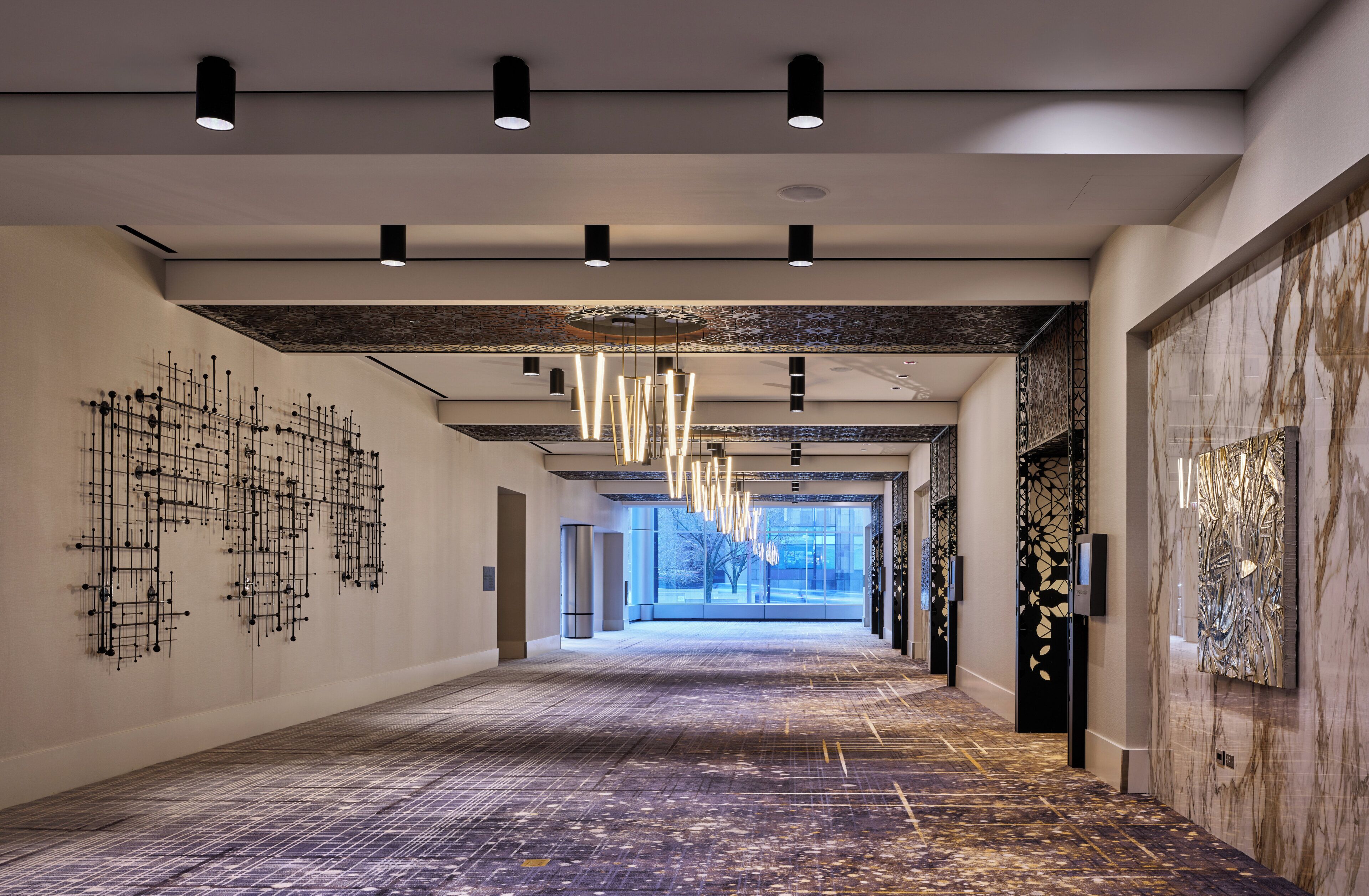 Ein moderner Hotelkorridor mit langer, gerader Gestaltung, eingelassener Beleuchtung und einem gemusterten Boden.