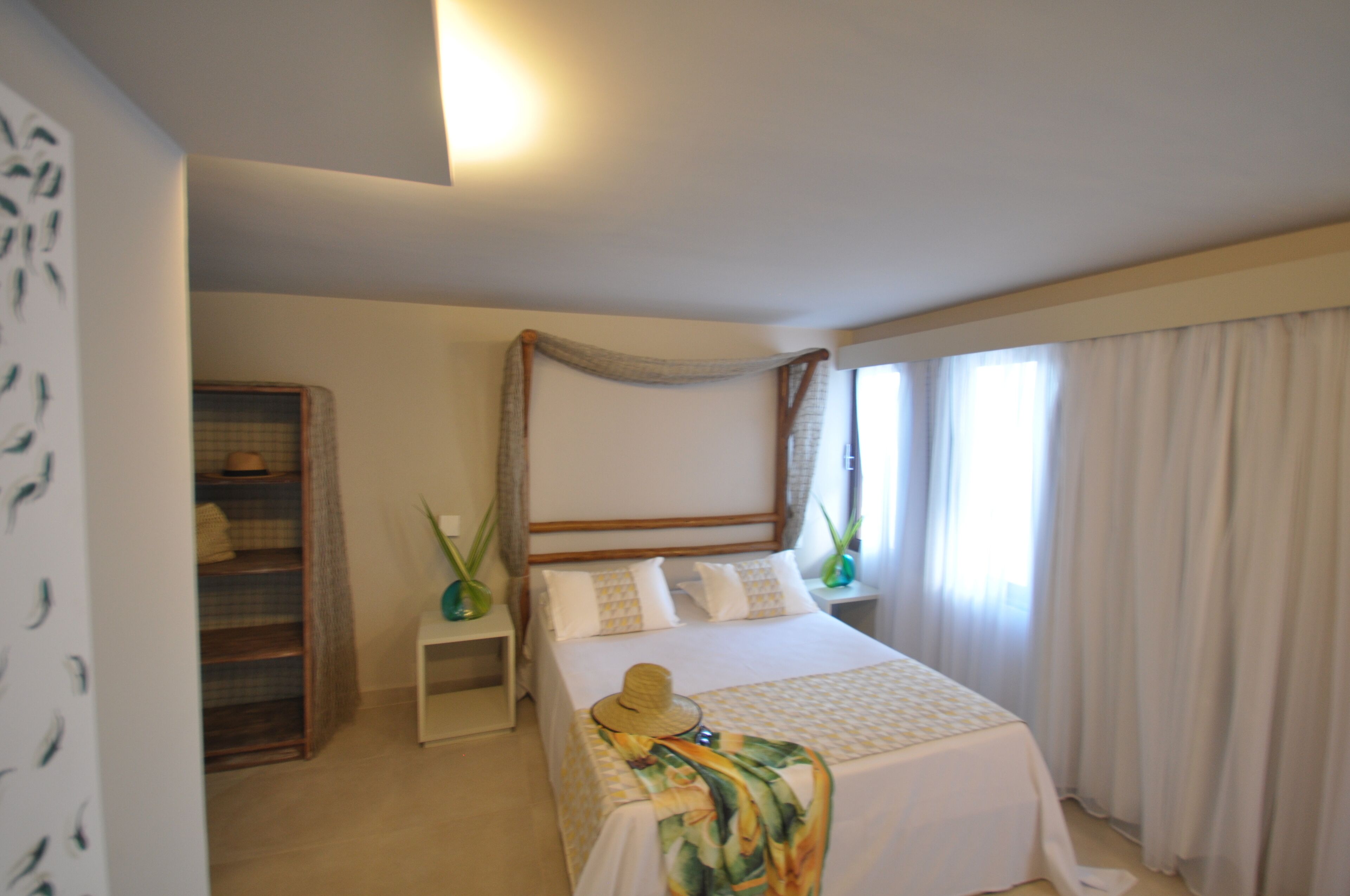 Une chambre à coucher bien rangée, avec un lit à baldaquin, une table de chevet ornée d’un vase et une armoire.