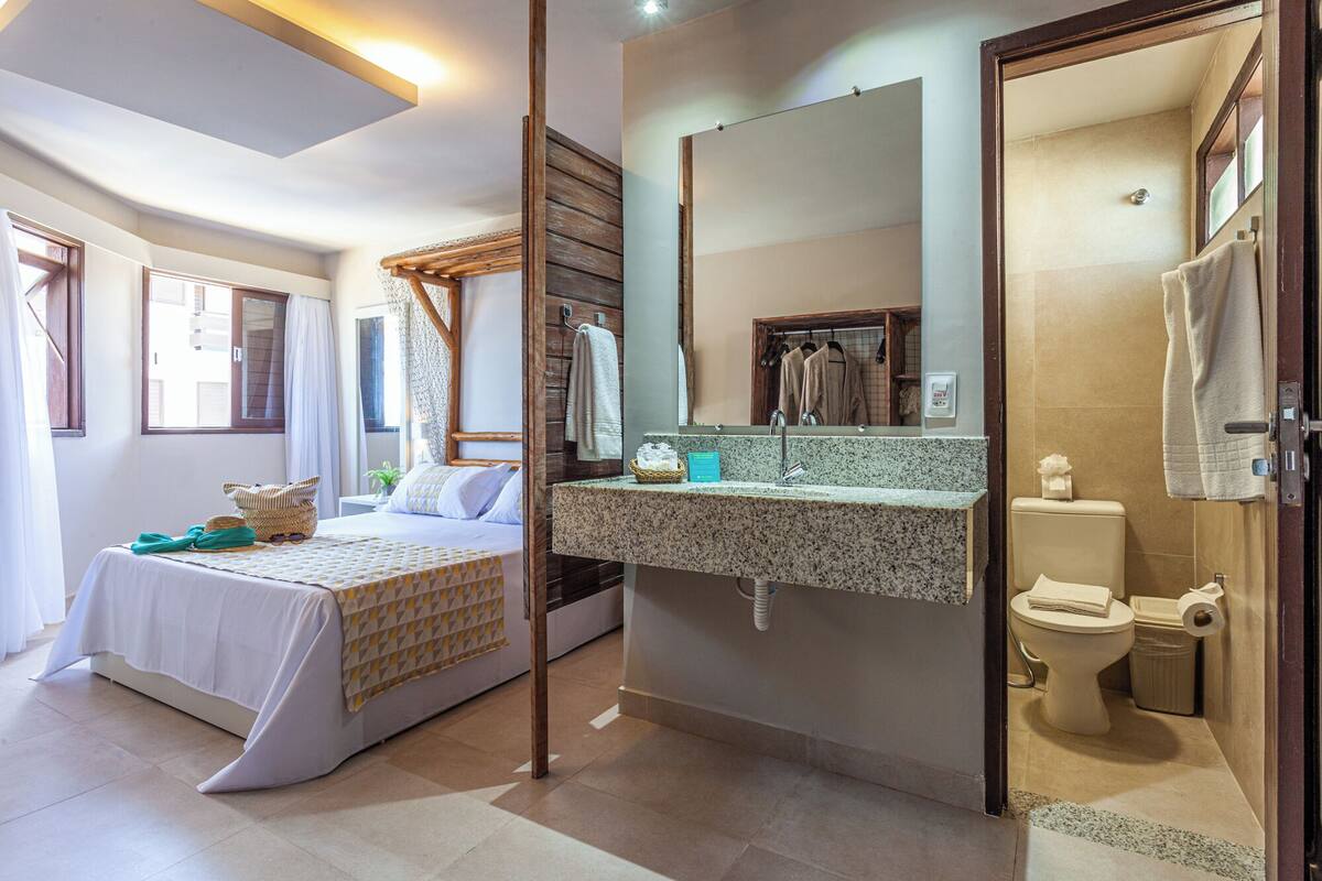 A hotel room with a bed, a bathroom with a sink and toilet, and a large mirror.